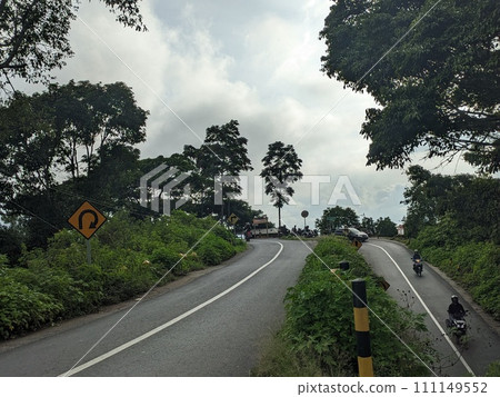 The road is in the middle of forests and mountains which are cloudy and cool 111149552