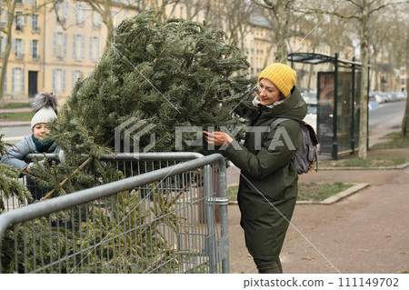 Mother and daughter throw away Christmas trees behind the fence Mother and daughter throw away Christmas trees behind the fence 111149702