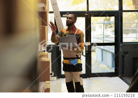 Storage room employee looking at cardboard boxes, checking merchandise checklist on tablet computer before start preparing customers orders. African american supervisor working in warehouse Storage room employee looking at cardboard boxes, checking merchandise checklist on tablet computer before start preparing customers orders. African american supervisor working in warehouse 111150218