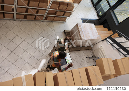 Diverse employees tracking clients online orders, checking warehouse logistics using laptop computer. Storage room supervisor preparing packages for delivery with manager. Top view concept Diverse employees tracking clients online orders, checking warehouse logistics using laptop computer. Storage room supervisor preparing packages for delivery with manager. Top view concept 111150280