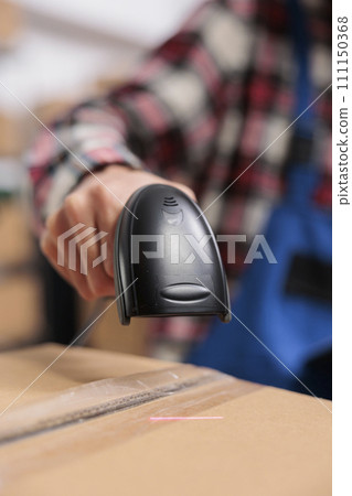 Delivery service employee scanning parcel and managing packages storing in warehouse. Storehouse worker doing shipment operations while holding barcode scanner in hand close up 111150368