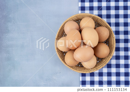 Top view of organic chicken eggs in wooden basket on blue wooden floor. 111153134