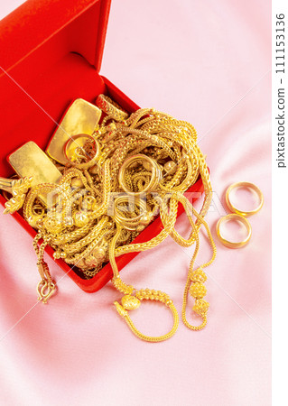 Many gold necklaces and gold bars in red box on velvet cloth background. Many gold necklaces and gold bars in red box on velvet cloth background. 111153136