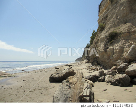 Waves lap on the beach with large rocks next to tall cliff 111154028