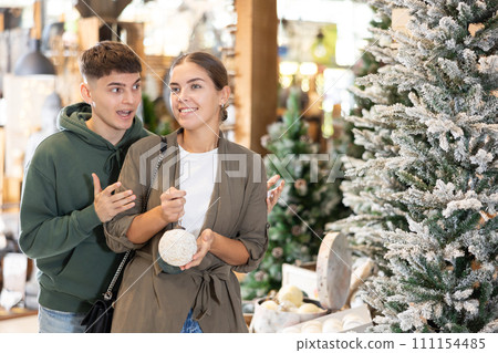 Girl with guy buyer considers New Year and Christmas decorations ornaments for Christmas tree 111154485