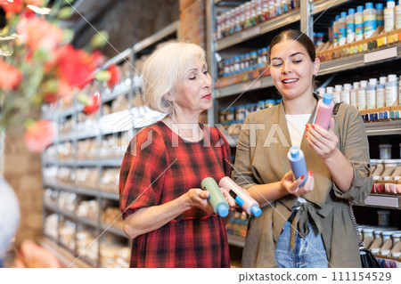 Two women consult with each other what pigment or acrylic varnish to choose for their future clay or ceramic dishes in specialized store 111154529