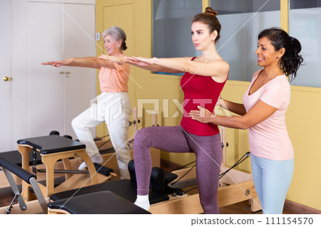 Young woman practicing pilates on wunda chair with Hispanic female trainer 111154570