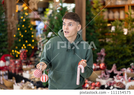 Young guy choosing christmas decorations in store Young guy choosing christmas decorations in store 111154575