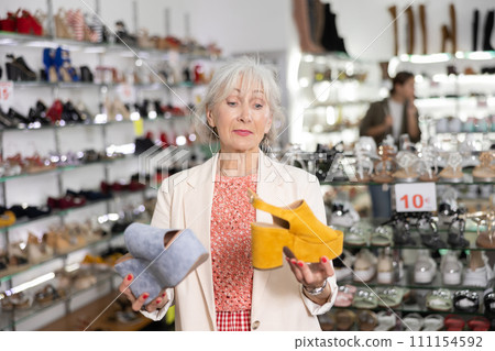 Senior female customer compare yellow and grey wedges sandals with backdrop on high platform 111154592