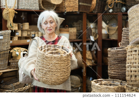 Senior woman looks at wicker basket in store. 111154624