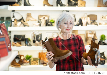Elderly woman chooses ankle boots in store 111154630