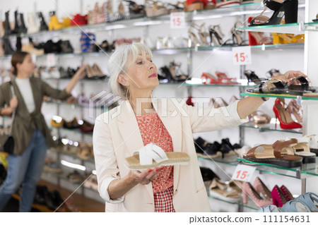 Mature woman who came to shoe store for shopping, chooses summer shoes 111154631