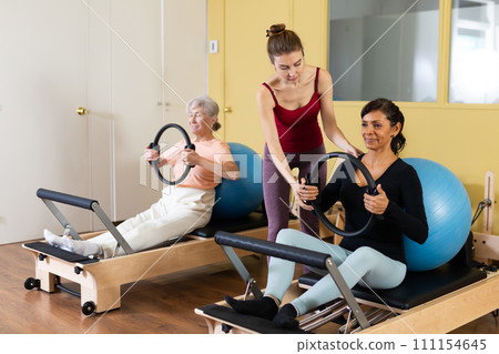 Two women perform an exercise using special rings and a fitball 111154645