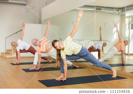 Three women standing in row and practicing yoga pose in studio Three women standing in row and practicing yoga pose in studio 111154838