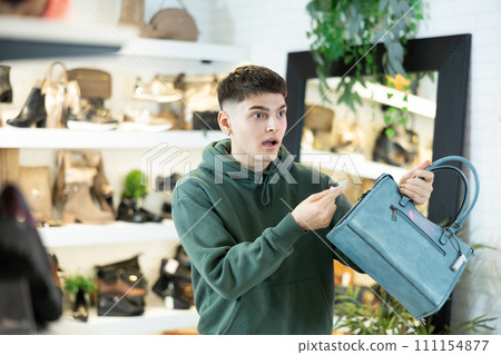 Guy customer is amazed to read price tag on leather handbag in store Guy customer is amazed to read price tag on leather handbag in store 111154877