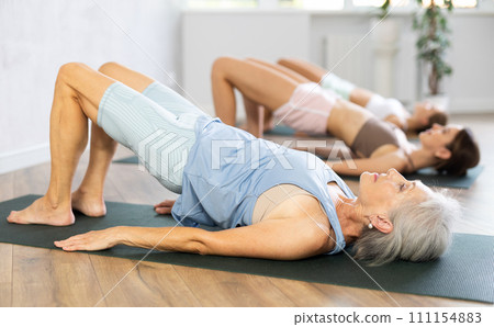 Senior woman performing shoulder supported bridge asana Sarvangasana 111154883