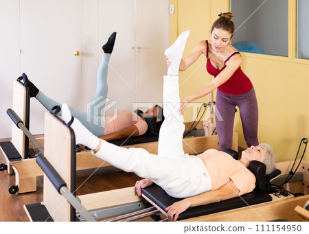 Female trainer helps a woman do stretching exercises Female trainer helps a woman do stretching exercises 111154950