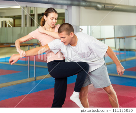 Girl practicing knee kick with arm hold to man in self defence training 111155030