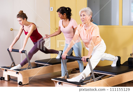 Two active women perform an exercise using a reformer bed 111155129