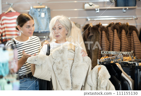 Girl consults with senior female friend about quality fur coat during shopping in clothes store 111155130