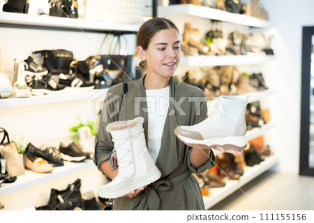 Girl buyer looks at footwear from new collection and picks up new pair of boots for winter. 111155156