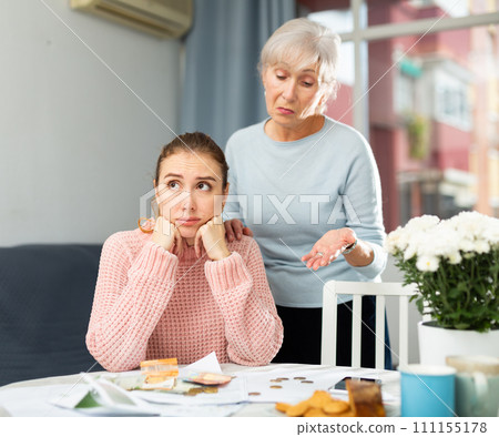 Frustrated girl and elderly woman counting cash at table at home 111155178