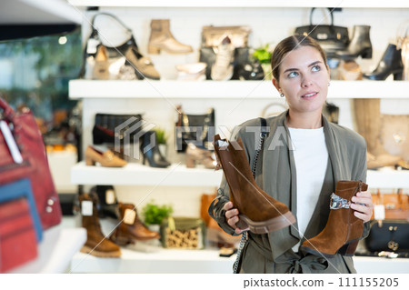 Girl buyer looks at footwear from new collection and picks up new pair of boots for winter. 111155205