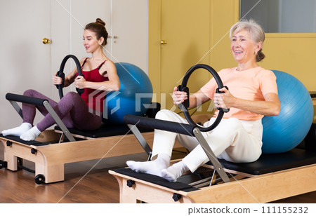 Elderly woman exercising with flex ring and fitball on pilates reformer Elderly woman exercising with flex ring and fitball on pilates reformer 111155232