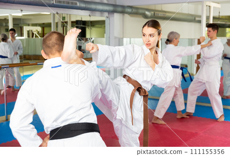 Young woman in kimono practicing heel kick paired with male opponent Young woman in kimono practicing heel kick paired with male opponent 111155356