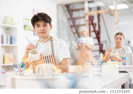 Focused guy enthusiastically painting on ceramic cup in pottery class Focused guy enthusiastically painting on ceramic cup in pottery class 111155505