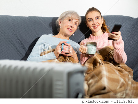 Relaxed elderly woman with adult daughter watching TV on sofa 111155633