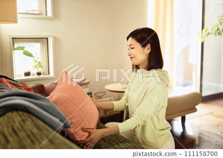 Middle-aged woman tidying up the living room Middle-aged woman tidying up the living room 111158700