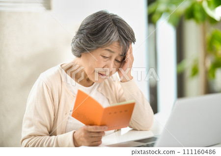 一位老年婦女一邊使用電腦，一邊查看她的退休金筆記型電腦 — 生命的終結 111160486