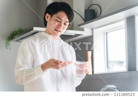 Sick man taking oral medicine, supplements, and medicines in the kitchen / Medication 111160523