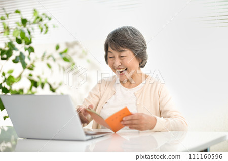 A senior woman using a computer while looking at her pension notebook, ending her life 111160596