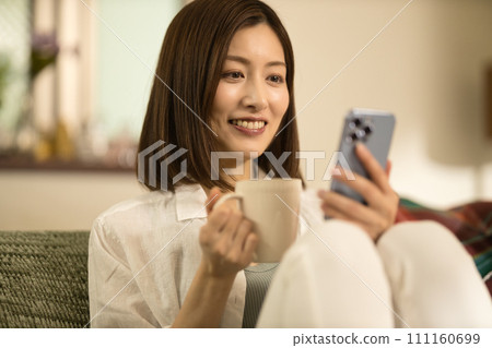 中年婦女在沙發上放鬆，喝咖啡，看著智慧型手機 111160699