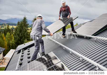 Professional technicians carrying solar PV battery. Engineers installing solar panel on a roof of house. Alternative resources and green energy concept. Professional technicians carrying solar PV battery. Engineers installing solar panel on a roof of house. Alternative resources and green energy concept. 111161505