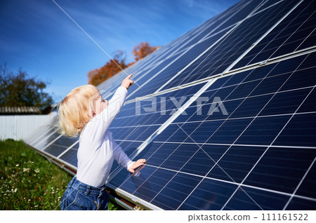 Little child looking at big solar panels. Interested boy investigates how does solar battery work. Small kid pointing at new panel. Concept of children and investment in renewable energy. 111161522