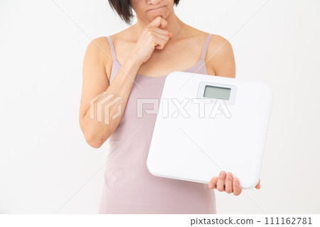 一名中年婦人拿著體重秤，憂心忡忡 111162781