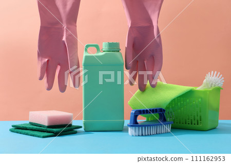 Colorful cleaning set for different supplies: green bottle container detergents, plastic basket with brushes, wiper, sponges and rubber gloves decorated on a pink background. Front view 111162953