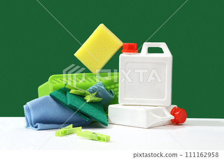 Creative ideas for advertising cleaning services and specialized detergents. White bottles with sponges, wiper and clothespin displayed on a green background. Front view, cleansing product 111162958
