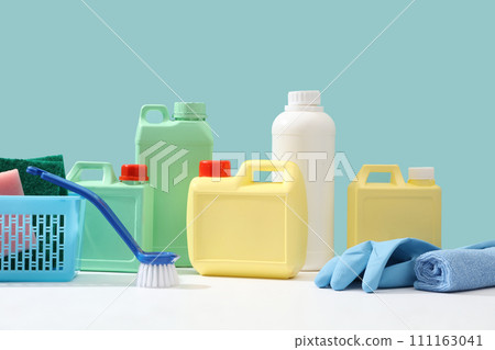 Cleanliness concept for advertising product. Front view of yellow, green and white plastic canisters decorated with blue cleaning equipment on pastel blue background. Minimal scene, space for design 111163041