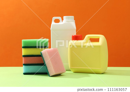 On the orange background and green plain, two detergent canisters blank label with stack of sponges displayed. Front view, mockup canister with space for design. Home cleaning products On the orange background and green plain, two detergent canisters blank label with stack of sponges displayed. Front view, mockup canister with space for design. Home cleaning products 111163057