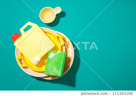 A bottle of detergent and a sponge are placed on top of a pile of dirty dishes on a turquoise background. Free space for text design and product display. 111163100