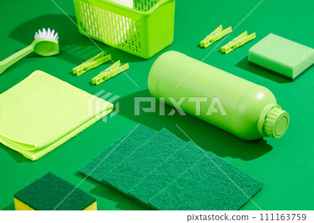 Green cleaning products on a plain green background. Unlabeled detergent bottle, rag, brush and sponges decorated. House Cleaning concept, scene for advertising Green cleaning products on a plain green background. Unlabeled detergent bottle, rag, brush and sponges decorated. House Cleaning concept, scene for advertising 111163759