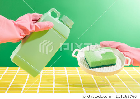 Ad template or package design for cleaning product. Hands wearing pink rubber gloves are holding a green plastic container containing detergent and sponge. Yellow ceramic background for mockup kitchen Ad template or package design for cleaning product. Hands wearing pink rubber gloves are holding a green plastic container containing detergent and sponge. Yellow ceramic background for mockup kitchen 111163766