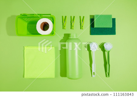 On a green background, items for cleaning the house are decorated. Empty detergent bottle, small brush, sponge and cleaning cloth. Top view, scene for advertising and space for design On a green background, items for cleaning the house are decorated. Empty detergent bottle, small brush, sponge and cleaning cloth. Top view, scene for advertising and space for design 111163843