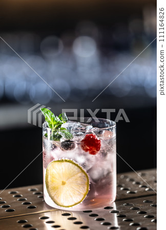 Pink cocktail Gin Tonic drink with raspberries, blueberries, lime and fresh mint 111164826