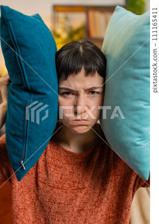 Irritated woman girl covers ears with cushions, annoyed by noisy neighbors suffers from headache 111165411