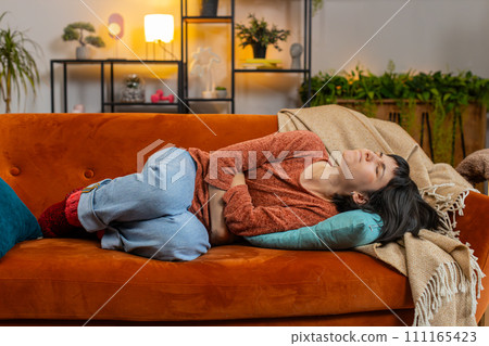 Upset woman embracing belly suffering from stomachache, menstrual painful feelings lying on sofa 111165423